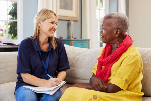 A smiling social worker sits on a couch with a client.