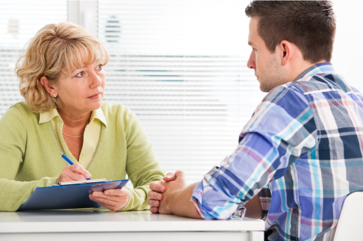 A social worker holding a clipboard talks with a client.